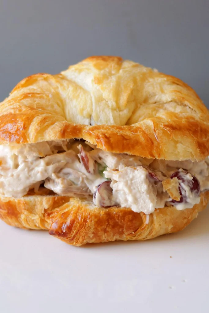A croissant chicken salad sandwich sitting on a white plate. A croissant chicken salad sandwich sitting on a white plate.