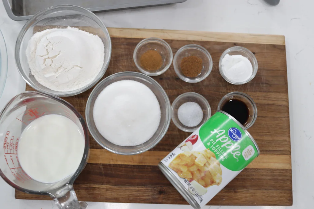 Several ingredients like flour, sugar, milk, etc., in glass bowls on a wooden cutting board. Several ingredients like flour, sugar, milk, etc., in glass bowls on a wooden cutting board.