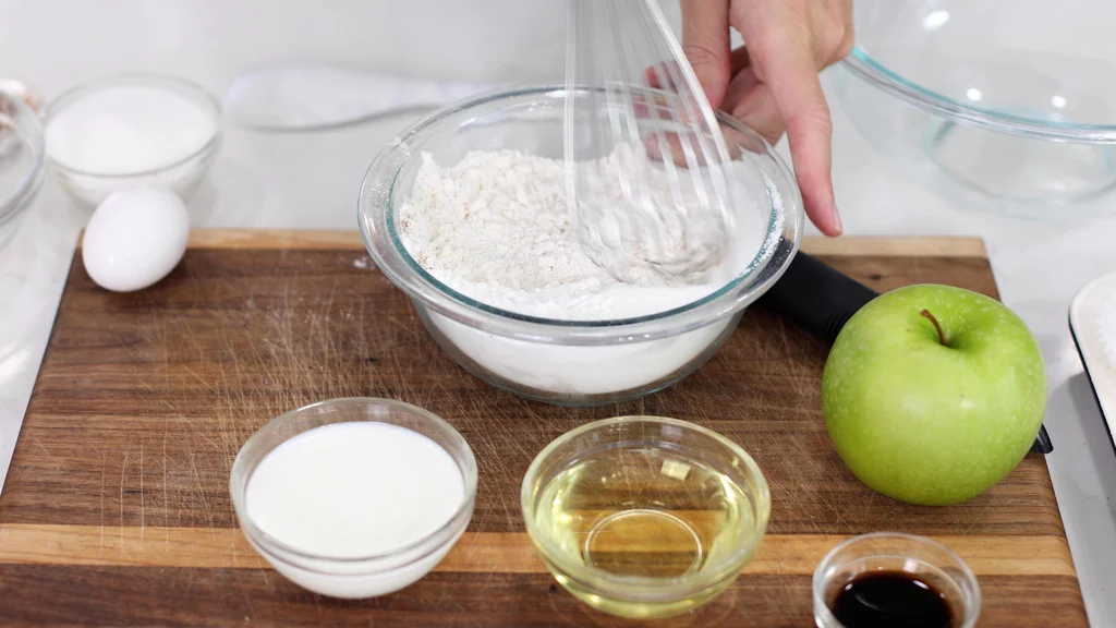 Hand whisking flour, sugar, baking powder and other ingredients in a glass bowl on top of a wooden cutting board. Hand whisking flour, sugar, baking powder and other ingredients in a glass bowl on top of a wooden cutting board.