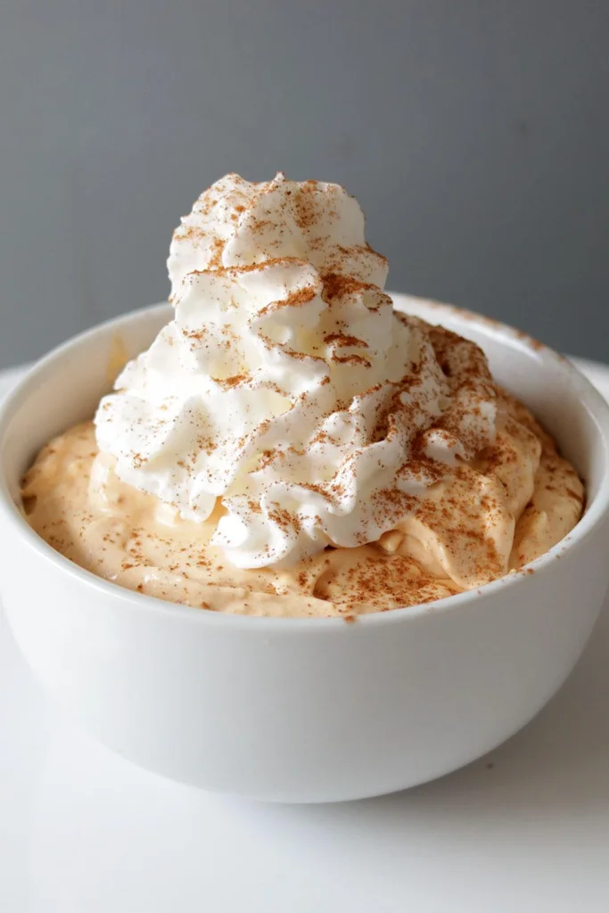 A white bowl with homemade no bake pumpkin pie filling topped with whipped cream and cinnamon. A white bowl with homemade no bake pumpkin pie filling topped with whipped cream and cinnamon.