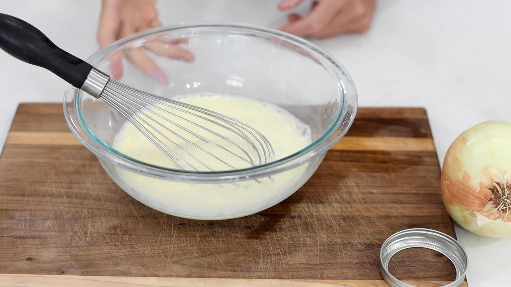 Hand whisking eggs, water, and milk together in a medium glass bow. Hand whisking eggs, water, and milk together in a medium glass bow.