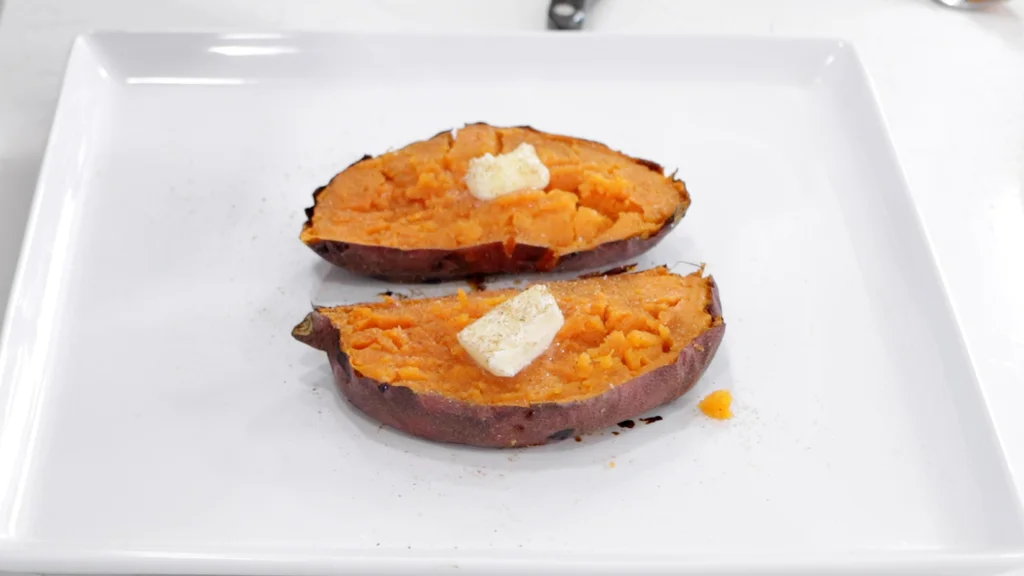Two sweet potato halves on a white plate with butter and cinnamon and sugar. Two sweet potato halves on a white plate with butter and cinnamon and sugar.