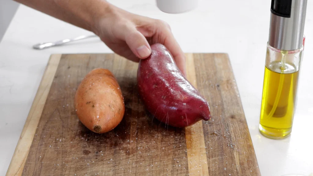 Hand holding a sweet potato that has been oiled and salted next to another one on a cutting board. Hand holding a sweet potato that has been oiled and salted next to another one on a cutting board.