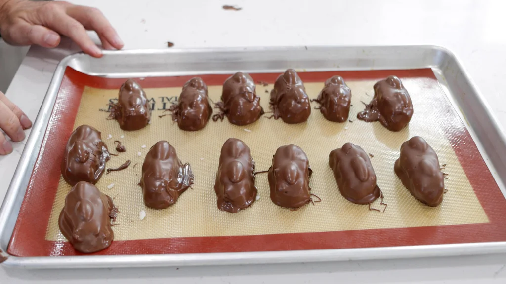 Several freshly dipped Homemade Almond Joys on a silicone mat on a sheet pan. Several freshly dipped Homemade Almond Joys on a silicone mat on a sheet pan.