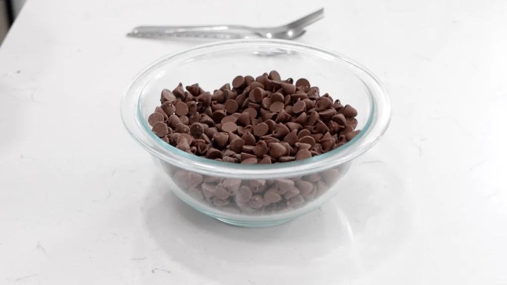 A medium bowl holding a bunch of milk chocolate chips. A medium bowl holding a bunch of milk chocolate chips.
