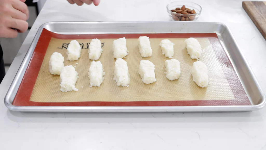 Several small coconut bars resting on a silicone baking mat on top of a sheet pan. Several small coconut bars resting on a silicone baking mat on top of a sheet pan.