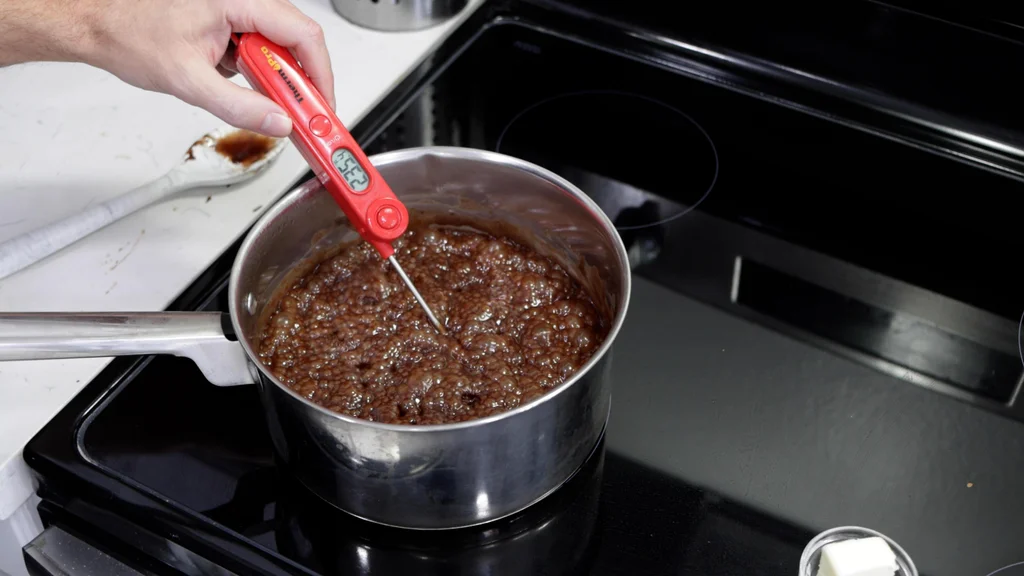 Hand holding a candy thermometer in a pot of boiling fudge. Hand holding a candy thermometer in a pot of boiling fudge.