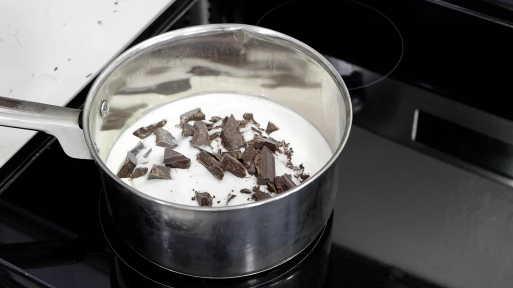 Cream, chocolate, and sugar in a stainless steel pot on a burner. Cream, chocolate, and sugar in a stainless steel pot on a burner.