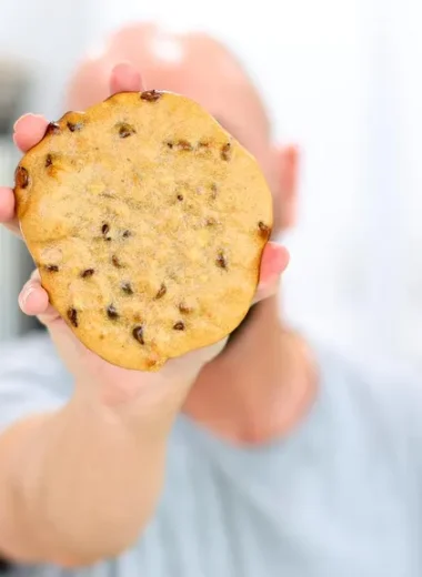 Hand holding a protein chocolate chip cookie towards the camera hiding his face.