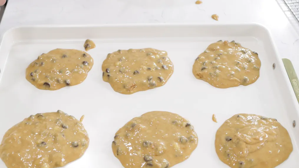 Six round protein chocolate chip cookies dough on a cream sheet pan. Six round protein chocolate chip cookies dough on a cream sheet pan.