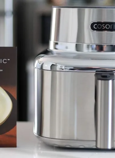 Cosori iconic stainless steel air fryer on a kitchen counter next to a cosori air fryer cookbook.