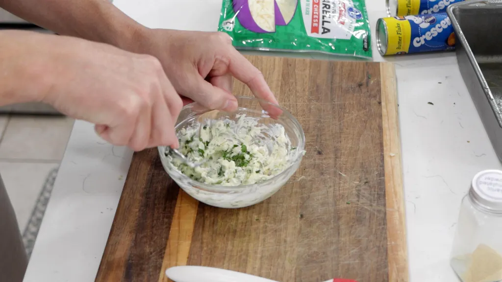 hand mixing butter, garlic, and parsley in a small glass bowl. hand mixing butter, garlic, and parsley in a small glass bowl.