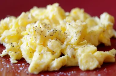A red plate with a pile of perfectly cooked scrambled eggs.